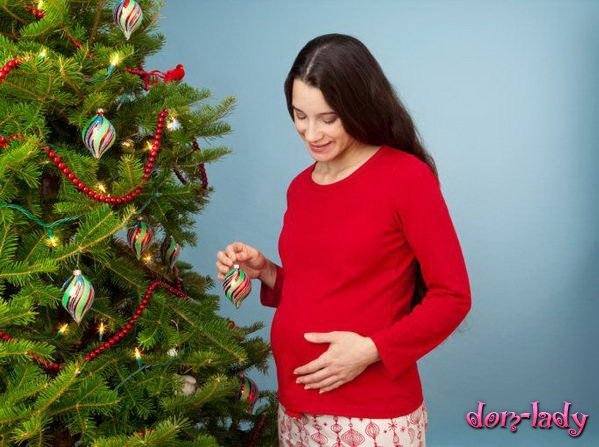 Беременная девушка наряжает елку